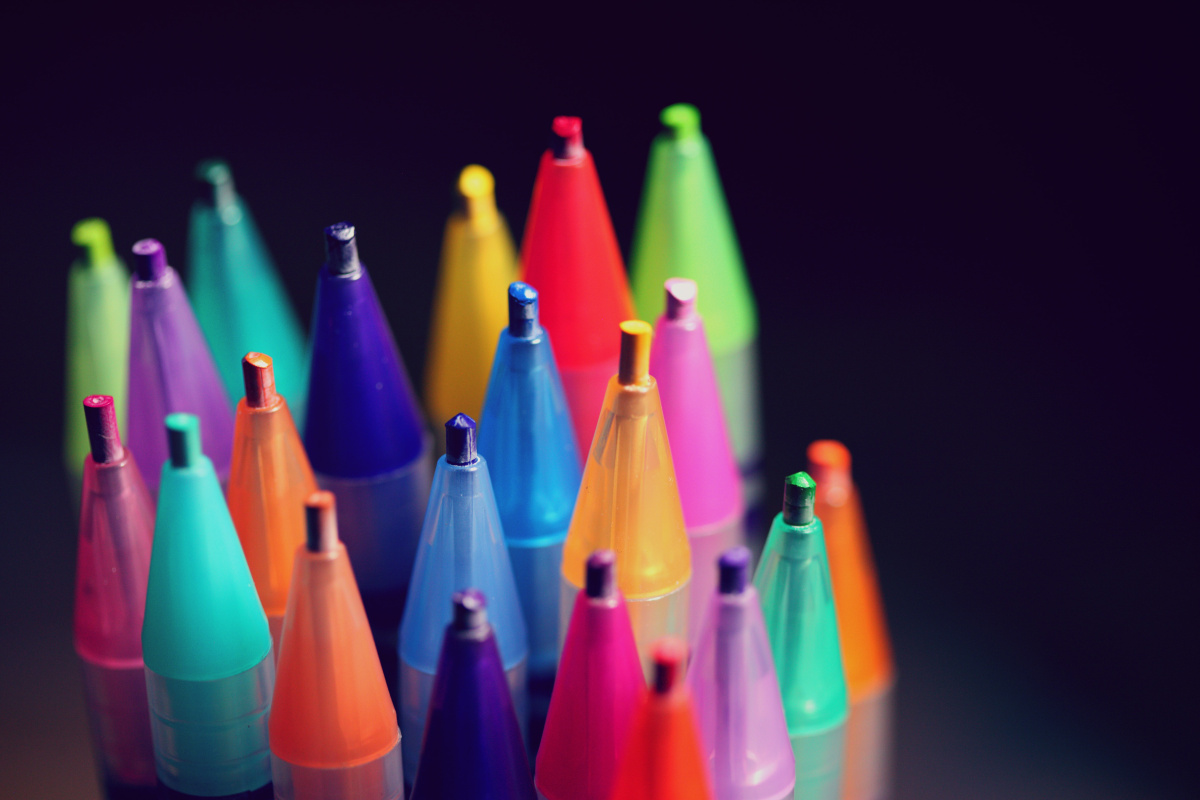 Mehrere bunte Stifte, die mit der Spitze nach oben zeigen, vor dunklem Hintergrund